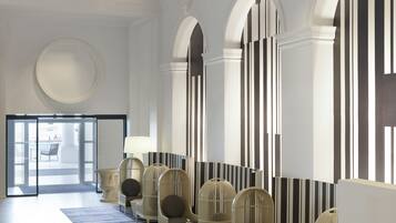 Een ruime lobby met een hoge plafond, een centraal zithoek met stoelen en een bank, een kamerbreed tapijt en een uitzicht door een glazen deur naar buiten.