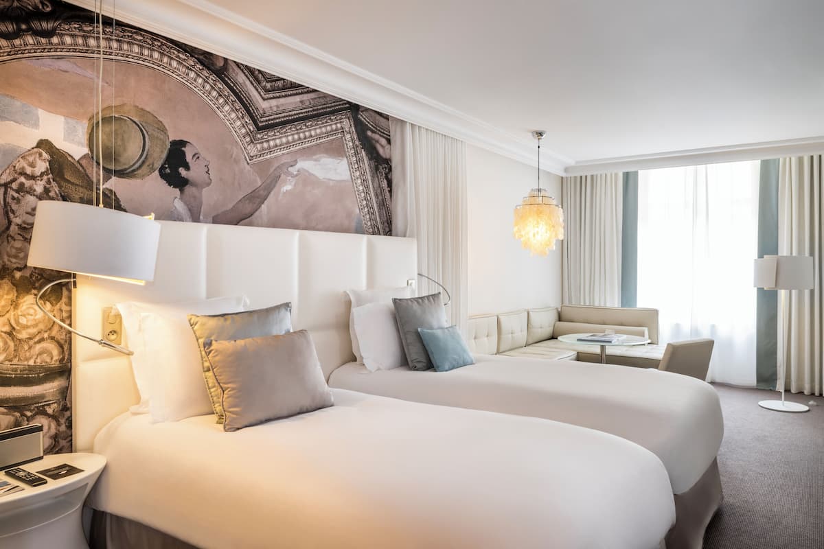 Une chambre d’hôtel avec deux grands lits, une petite table, une chaise, un bureau et une grande fresque murale.
