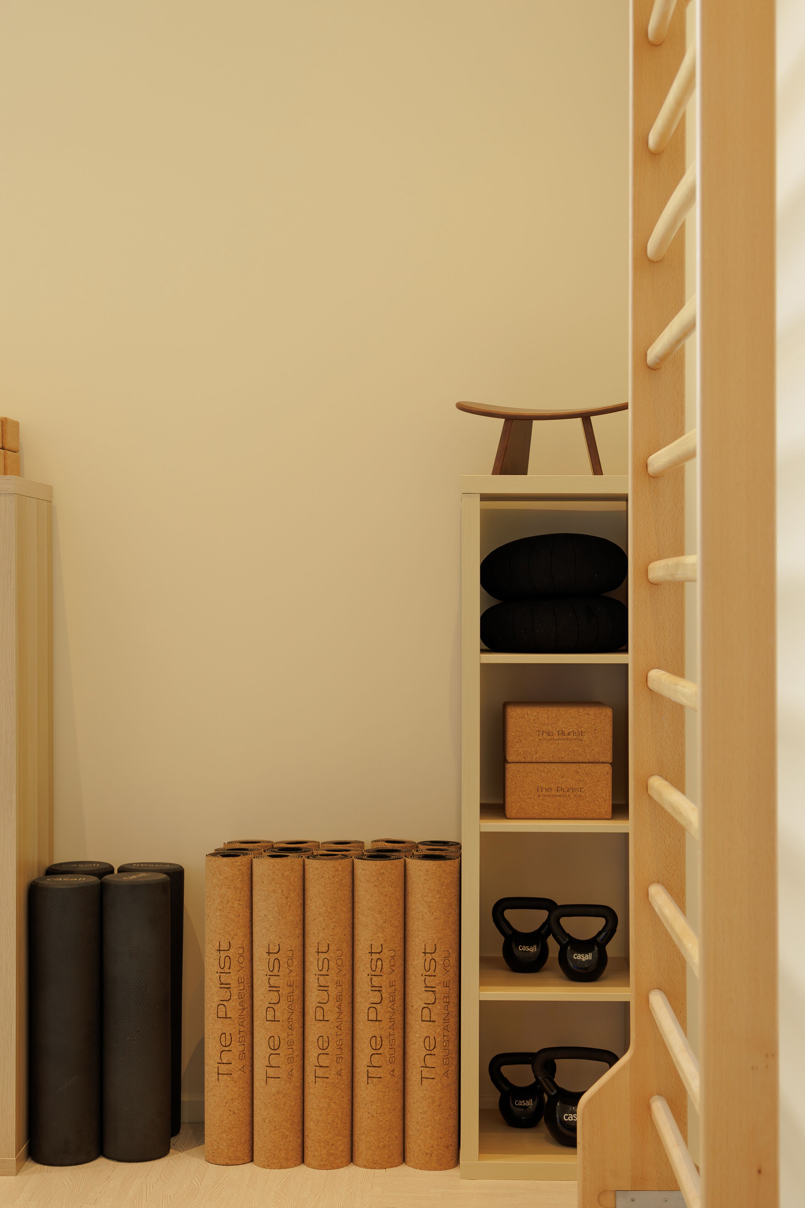 A minimalist room with a wooden wardrobe, a shelf with black kettlebells, and a pair of black shoes.