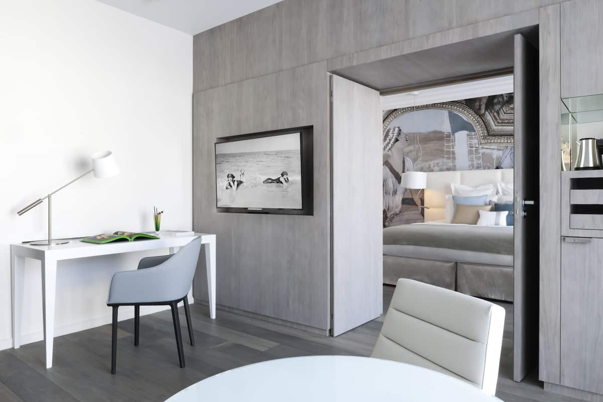 Une chambre d’hôtel moderne avec un bureau blanc, un canapé confortable et une grande fenêtre donnant sur le paysage urbain.