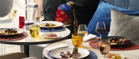 A dining table with multiple plates of food, glasses of wine, and a colorful pillow in the background.