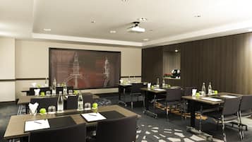 A conference room with multiple tables, chairs, and a large screen displaying an image of a building.