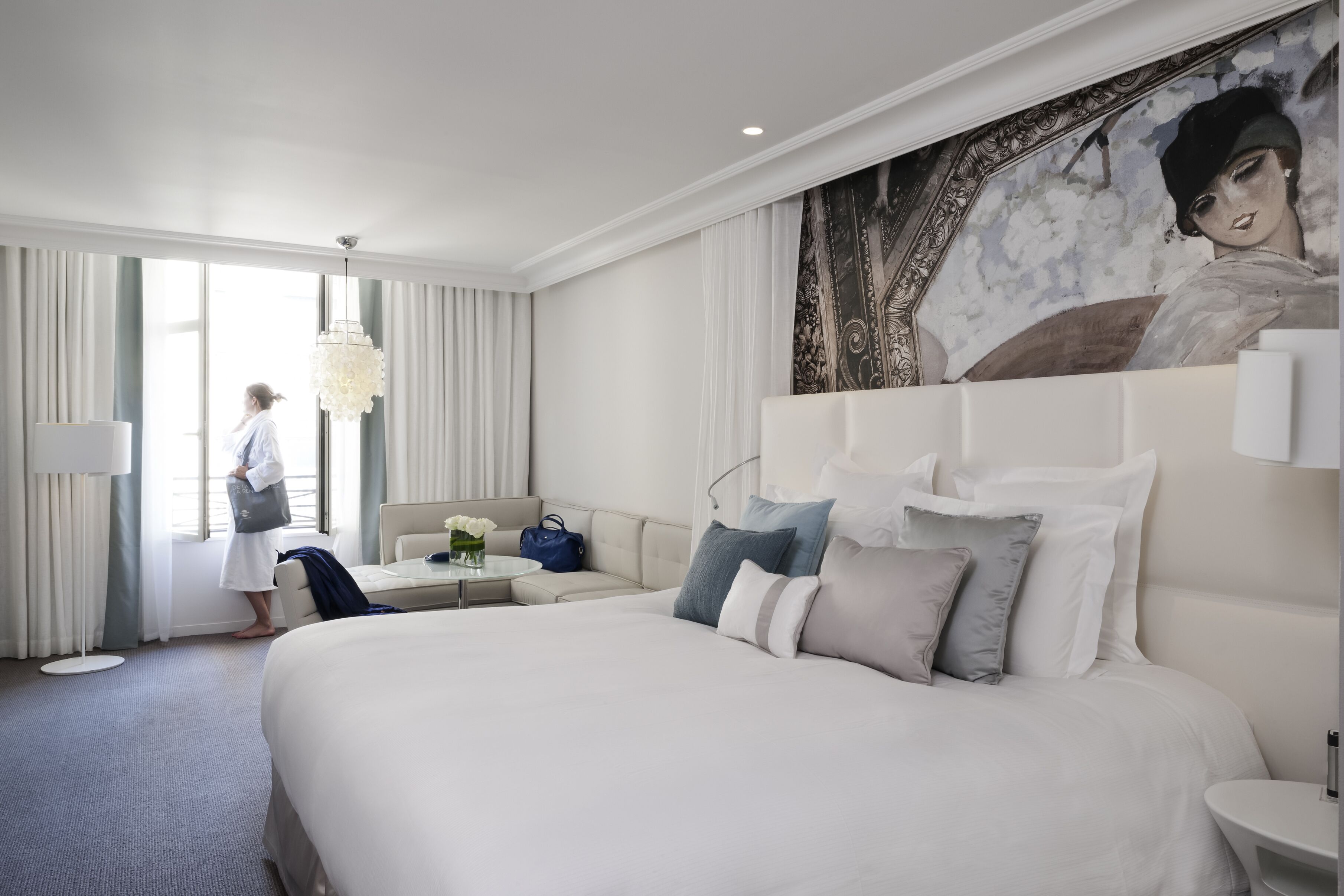 A modern hotel room with a large bed, a seating area, and a painting on the wall.