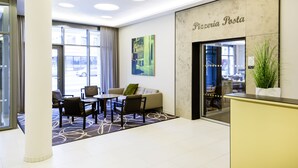 A modern reception area with a sofa, chairs, and a table. There is a large window with curtains, a reception desk, and a wall-mounted sign that reads "Pizzeria Posta". - Novotel Nuernberg Centre Ville (Nuremberg)
