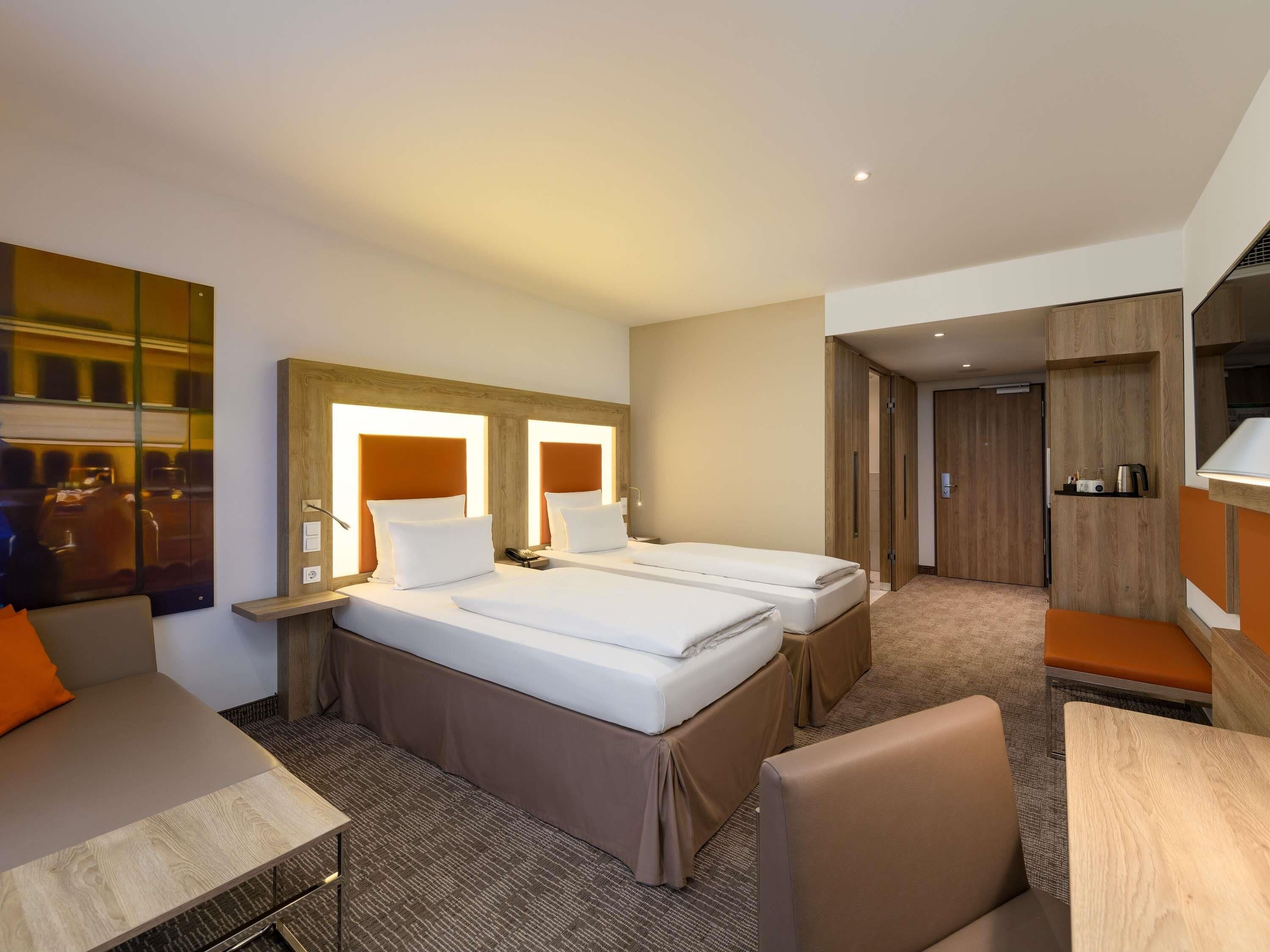 A hotel room with two beds, a desk, a chair, and a large mirror.