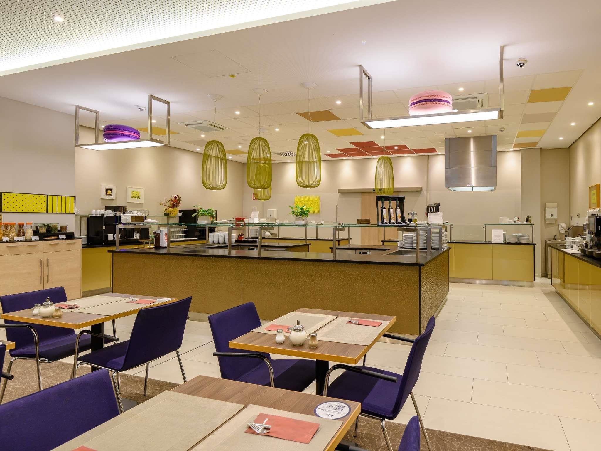 A modern dining area with tables, chairs, and a kitchen in the background.