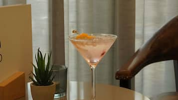 Ein Martini-Glas mit Orangenscheibe auf einem runden Tisch, eine kleine Topfpflanze und ein Glas Wasser.