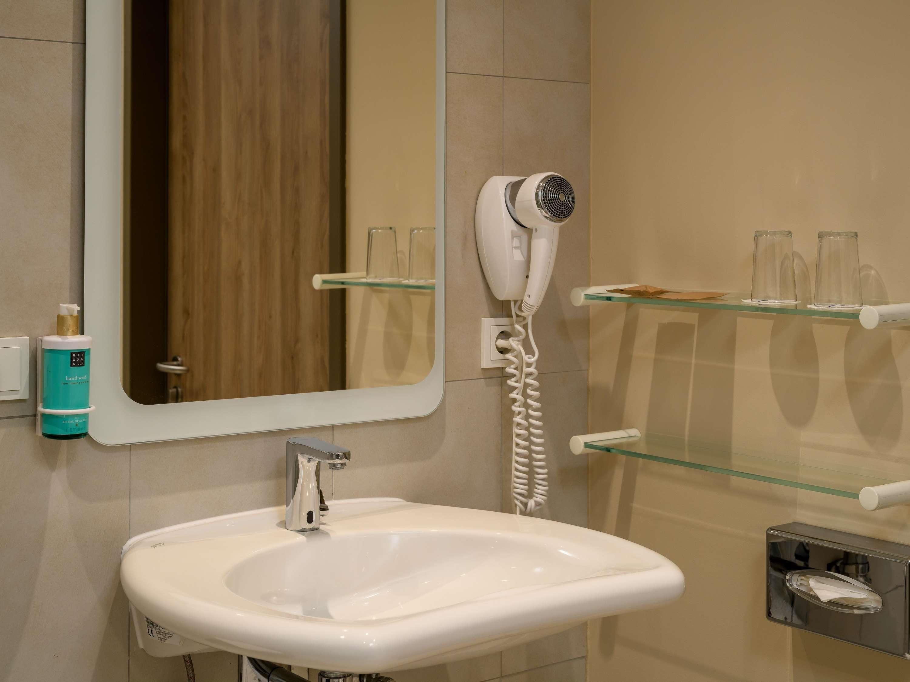 Un baño con lavamanos blanco, secador de pelo y espejo.