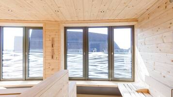 Eine Holzhütte mit großen Fenstern, einer Bank und Blick auf eine verschneite Landschaft.
