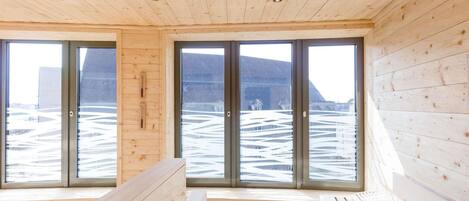 Una cabaña con paredes de madera y ventanas amplias, un banco y vistas a un paisaje nevado.