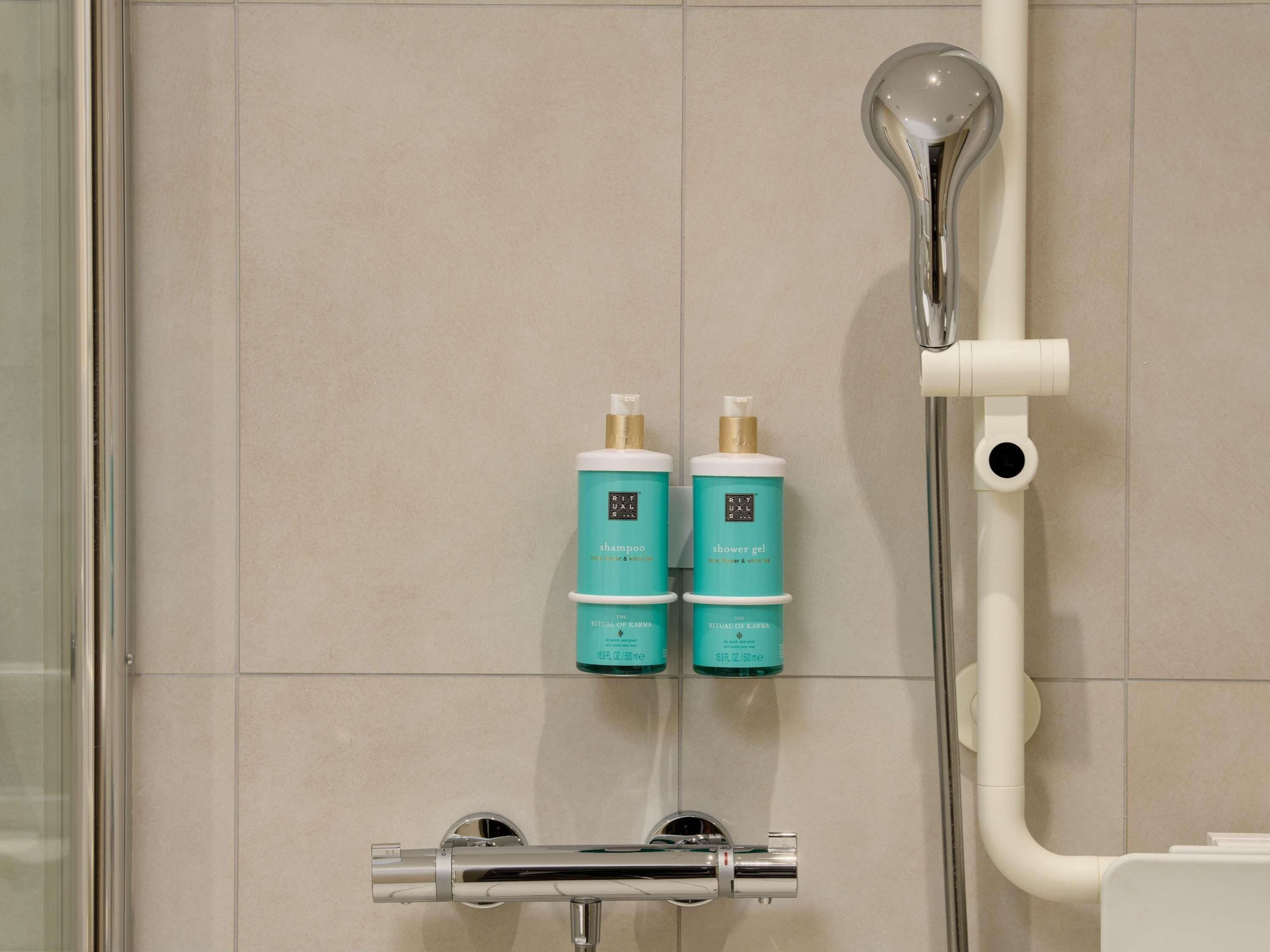 Eine Dusche mit Handbrause sowie zwei Flaschen Karma Ritual Shampoo und Duschgel.