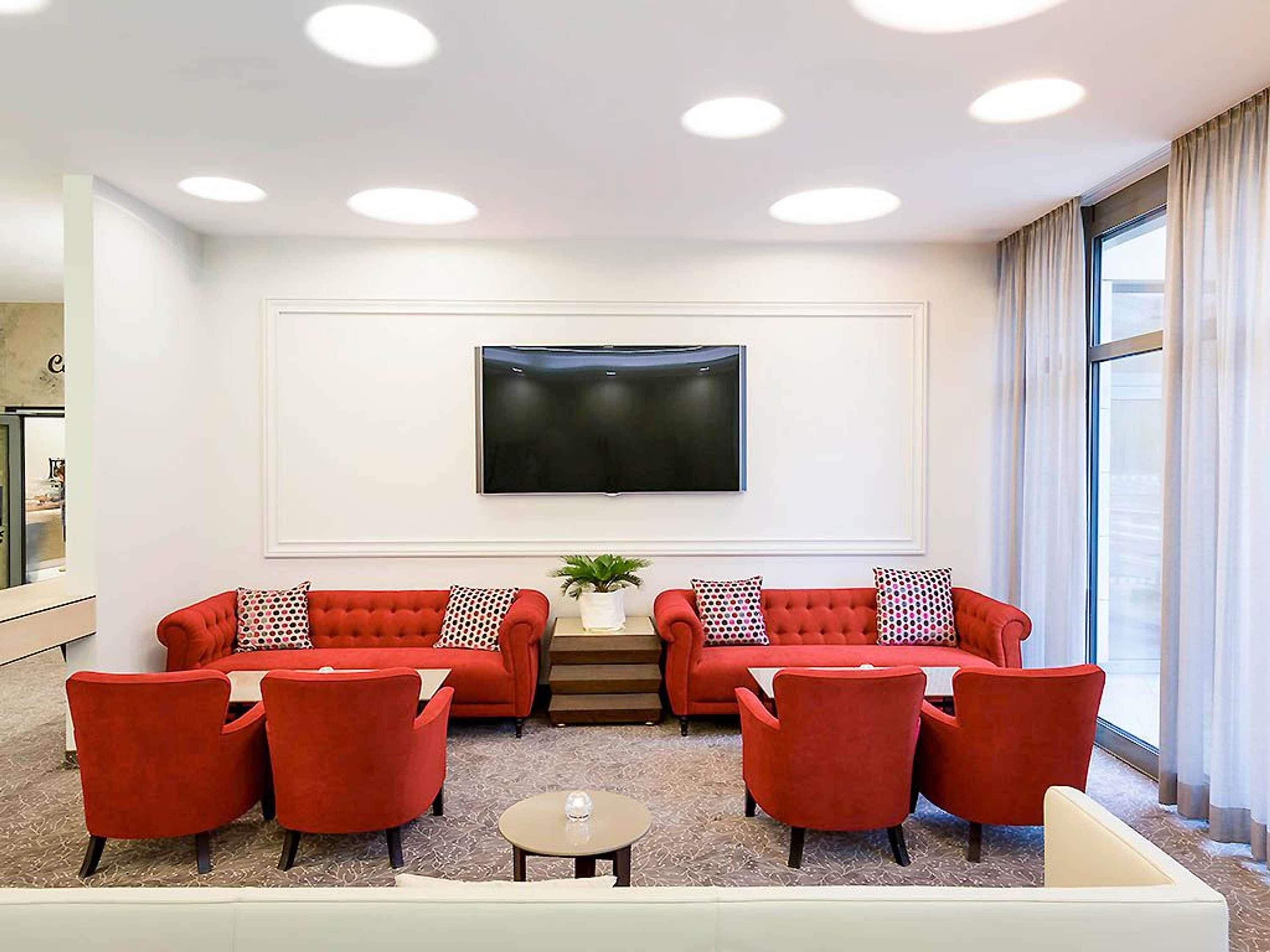 A modern living room with two red sofas, a coffee table, and a flat-screen TV mounted on the wall.
