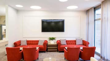 A modern living room with two red sofas, a coffee table, and a flat-screen TV mounted on the wall.