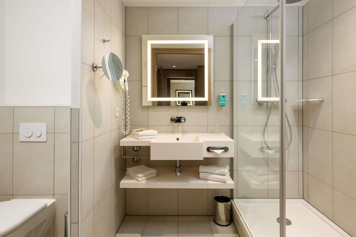 A modern bathroom with a glass shower enclosure, a white sink with a mirror, and a towel rack.