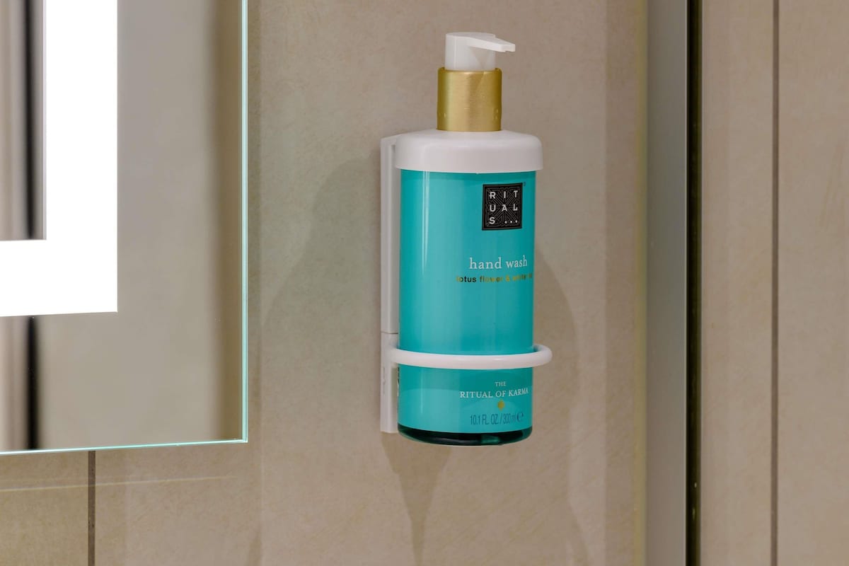 A hand wash dispenser in a bathroom with a teal and white color scheme.
