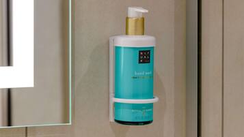 A hand wash dispenser in a bathroom with a teal and white color scheme.