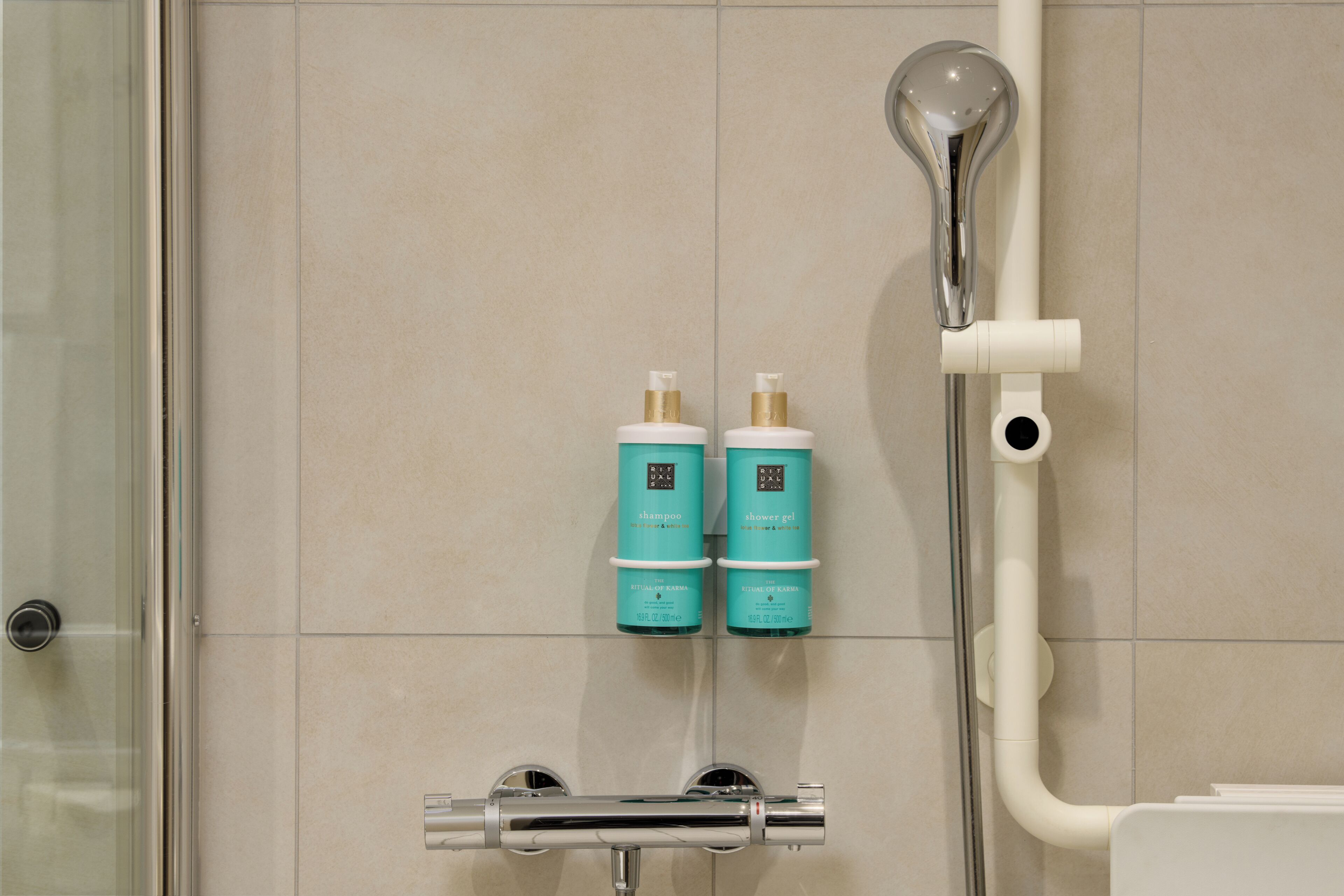 Une douche équipée d’un pommeau de douche à main et d’une étagère murale sur laquelle sont posés deux flacons de shampoing et de gel douche.