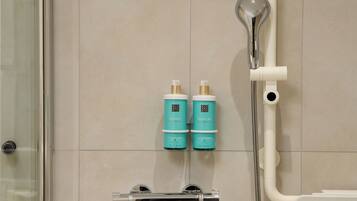 Eine Dusche mit Duschbrause, zwei Shampoo- und Duschgel-Flaschen auf einem Wandregal.