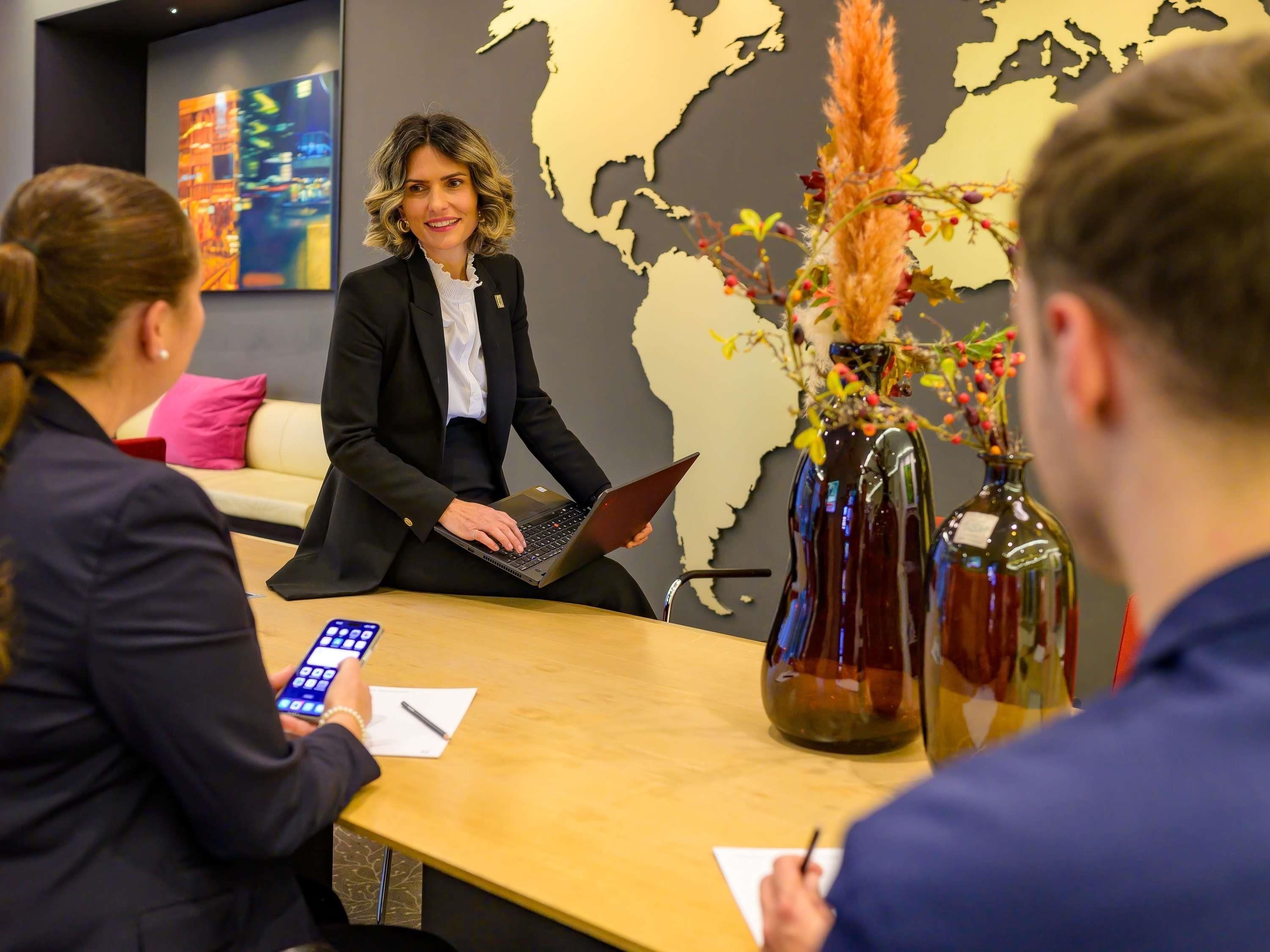 A professional setting with a seated woman using a laptop, a world map on the wall, and decorative vases on the table.