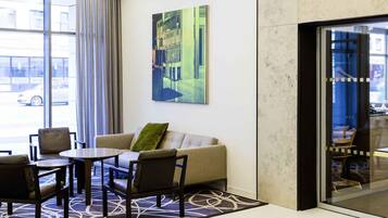 A hotel lobby with a sofa, chairs, a table, a large window, and a painting.