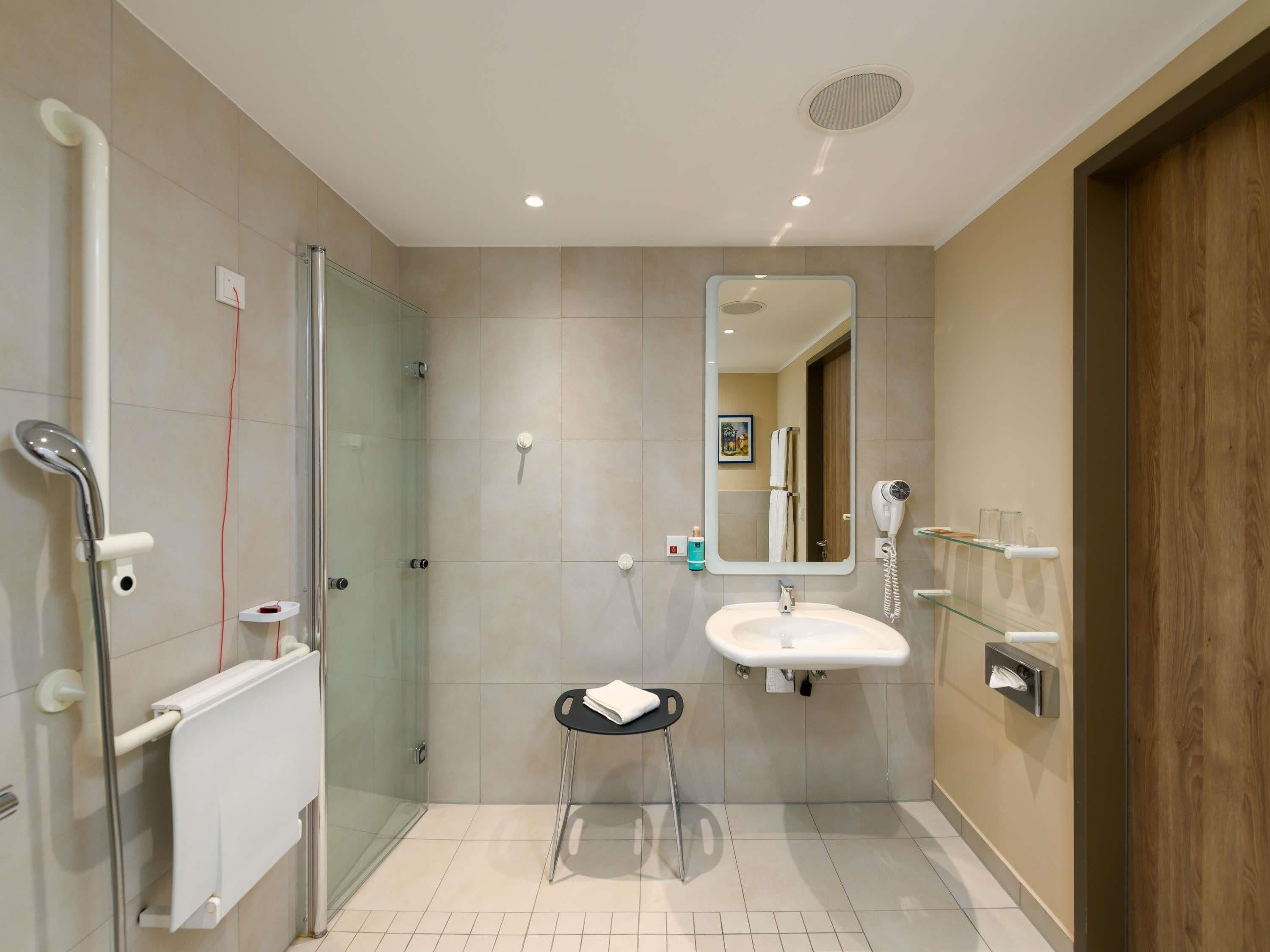 Ein modernes Badezimmer mit Duschkabine aus Glas, Waschbecken mit Spiegel und einem kleinen Hocker.