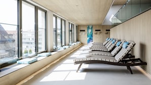 A modern interior with a long bench seating area along a large window, a wooden ceiling, and a city view. - Novotel Nuernberg Centre Ville (Nuremberg)