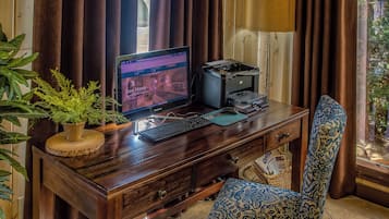 A wooden desk with a computer monitor, keyboard, and printer. There is a blue patterned chair and a potted plant on the desk.