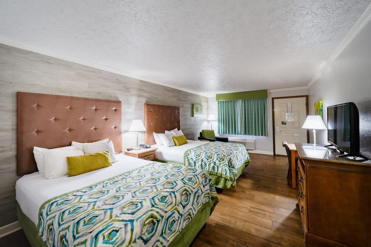 Een hotelkamer met drie bedden, een televisie, een bureau en een stoel.