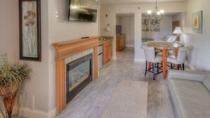 A modern living room with a fireplace, a dining area with a round table and chairs, and a TV mounted on the wall. - Accommodation By Willow Brook Lodge (Pigeon Forge)