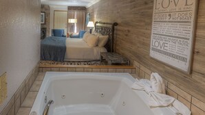 A hotel room with a large bathtub, a bed with a blue bedspread, and a wall with a love-themed quote. - Accommodation By Willow Brook Lodge (Pigeon Forge)