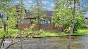 A lodge with a brick facade and large windows, situated by a flowing river with surrounding greenery. - Accommodation By Willow Brook Lodge (Pigeon Forge)