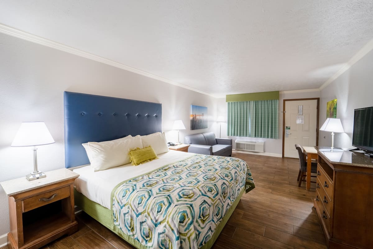 Een hotelkamer met een bed, nachtkastjes, een bureau, een stoel, een televisie en een raam met gordijnen.