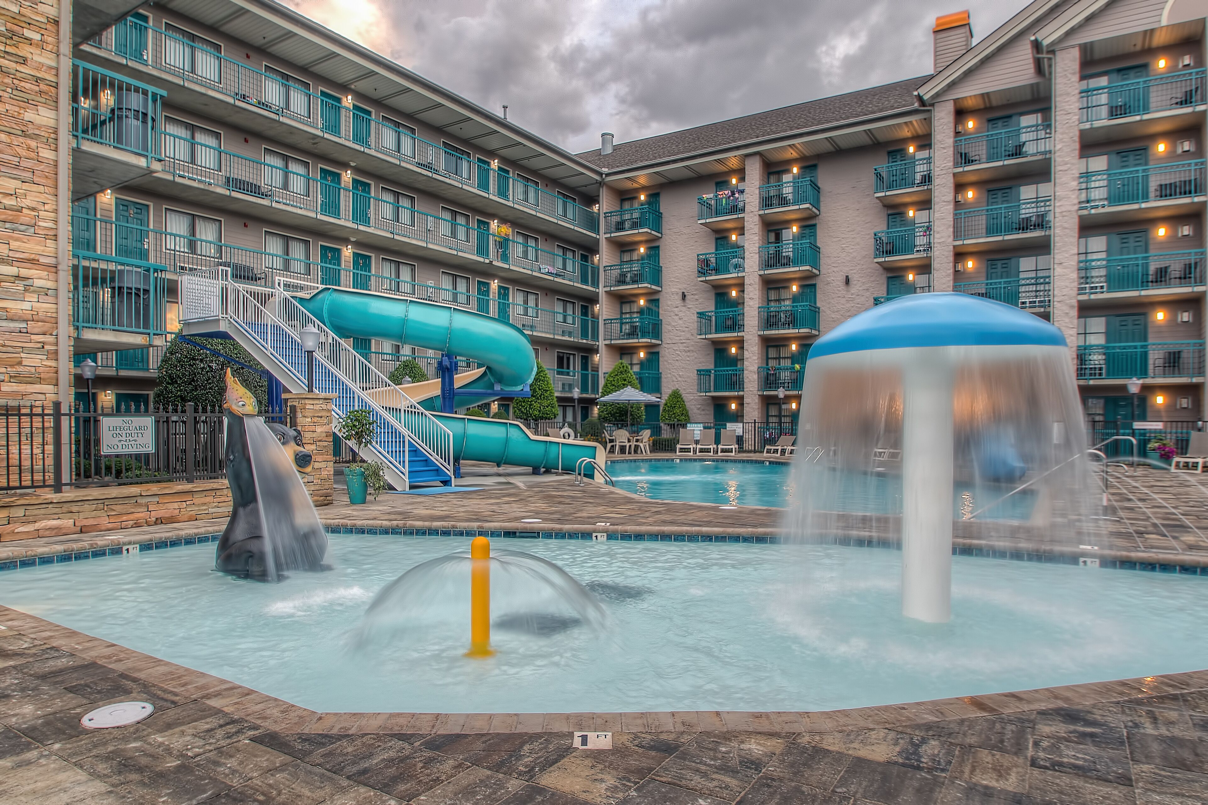 Zona de piscina de hotel con tobogán de agua, fuente y solárium.