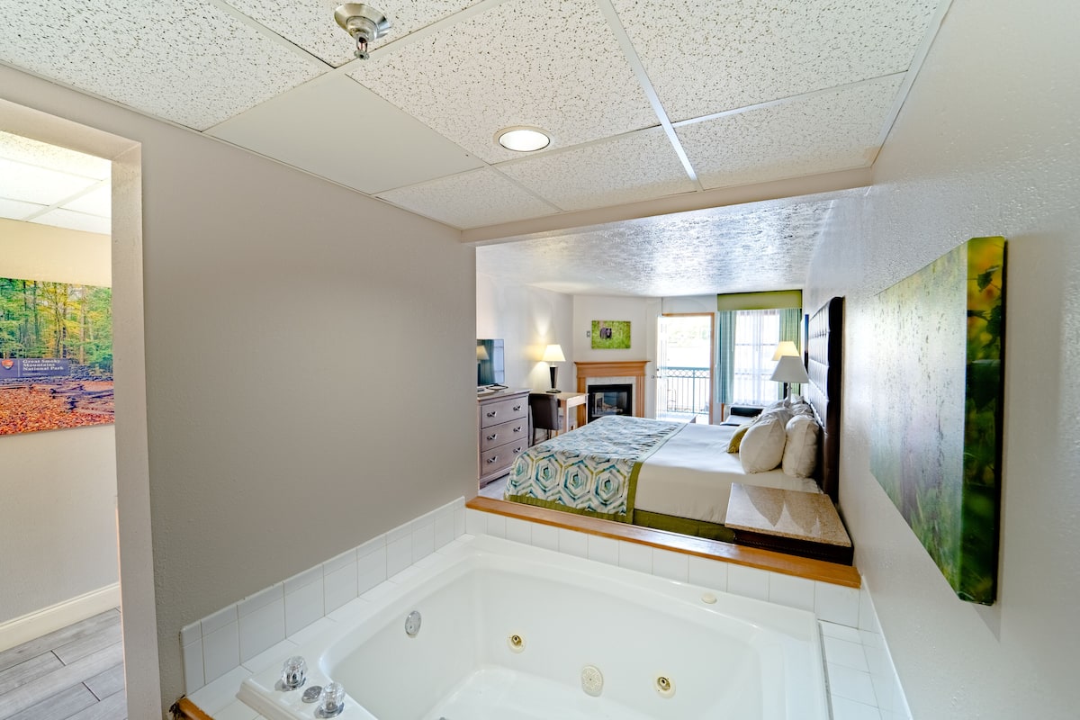 Een moderne slaapkamer met een groot, wit bad en een bed met een bedsprei met een patroon, plus een schilderij aan de muur.