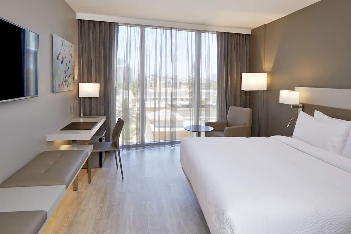 A modern hotel room with a large bed, a desk, a chair, and two lamps.