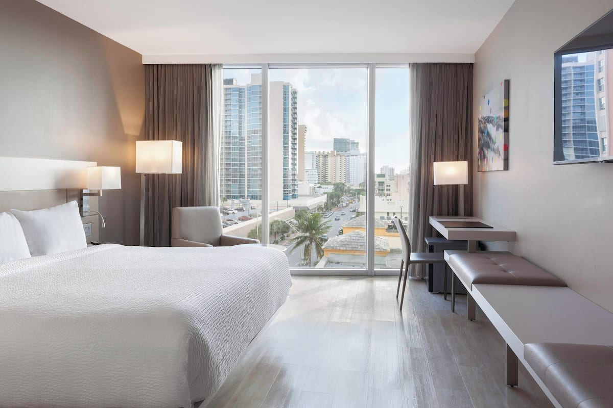 A hotel room with a large bed, a desk, and a view of the cityscape.