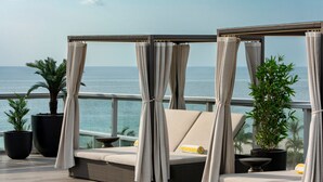 A balcony with a wicker sofa, two potted plants, and a view of the sea. - AC Hotel by Marriott Miami Beach (Miami Beach)