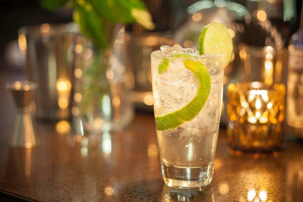 Un vaso de una bebida transparente con hielo y una rodaja de lima sobre una barra.