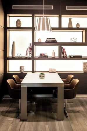 A modern dining area with a white table and brown chairs, a bookshelf with books and decorative items, and a large window with natural light. - AC Hotel by Marriott Miami Beach (Miami Beach)