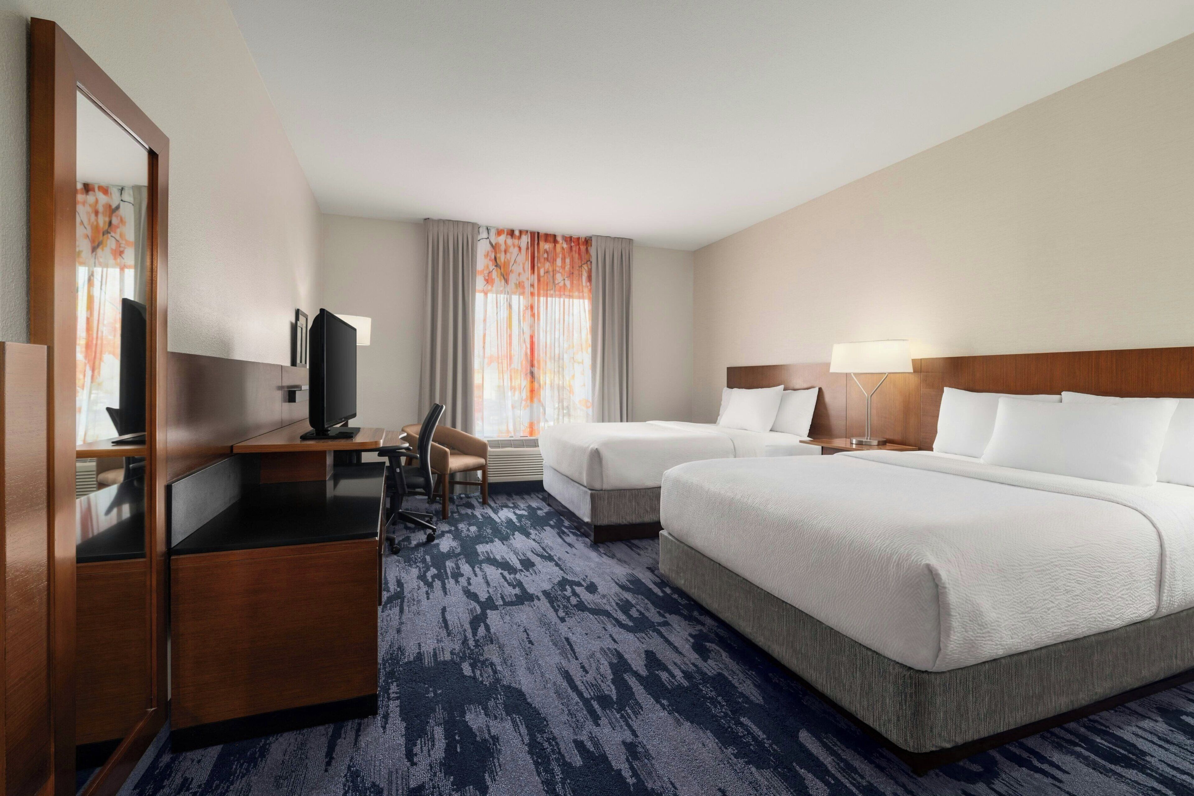 A hotel room with a bed, a desk, a chair, a television, and a large mirror.