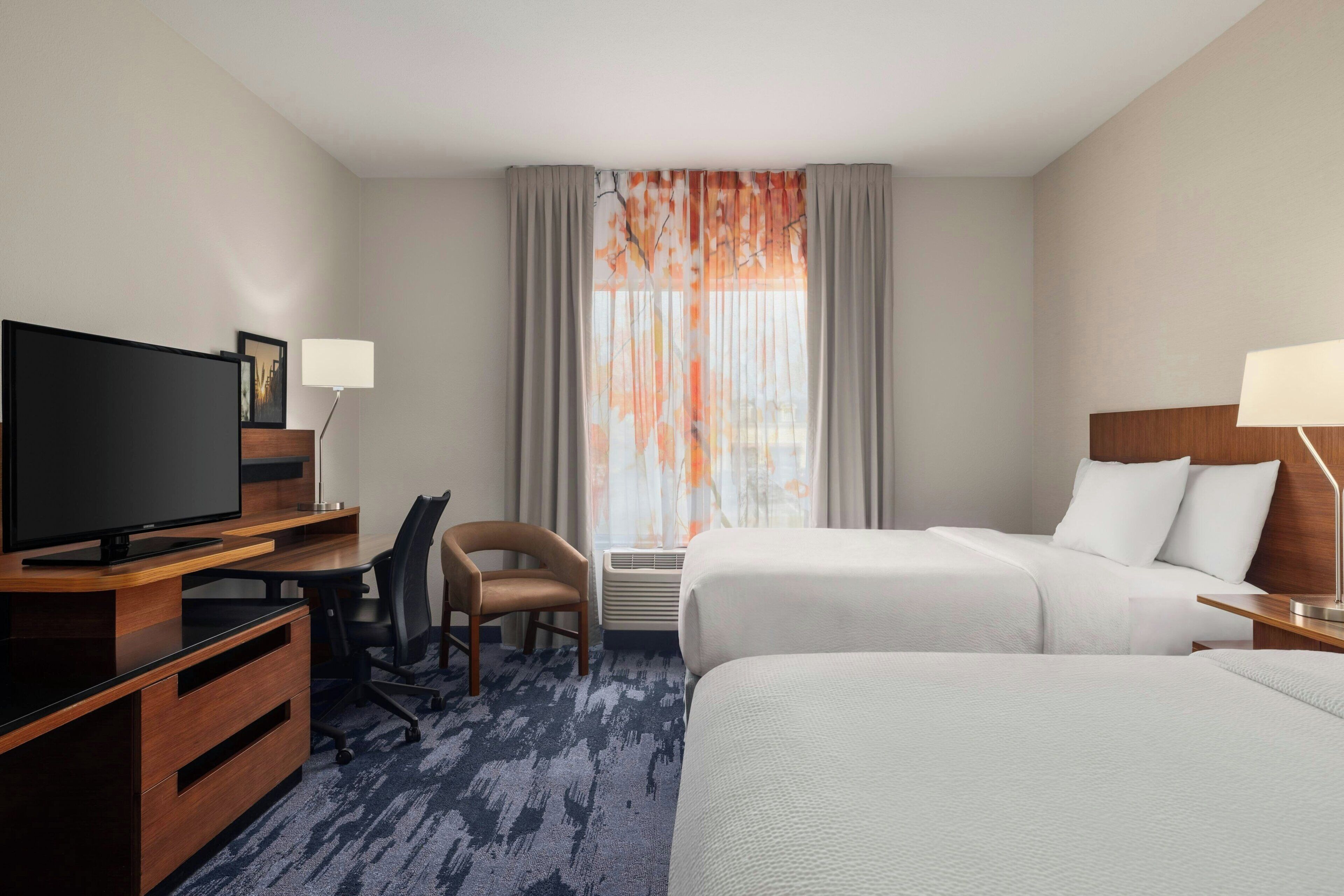 Een hotelkamer met een bed, een bureau met een televisie, een stoel en een raam met gordijnen.