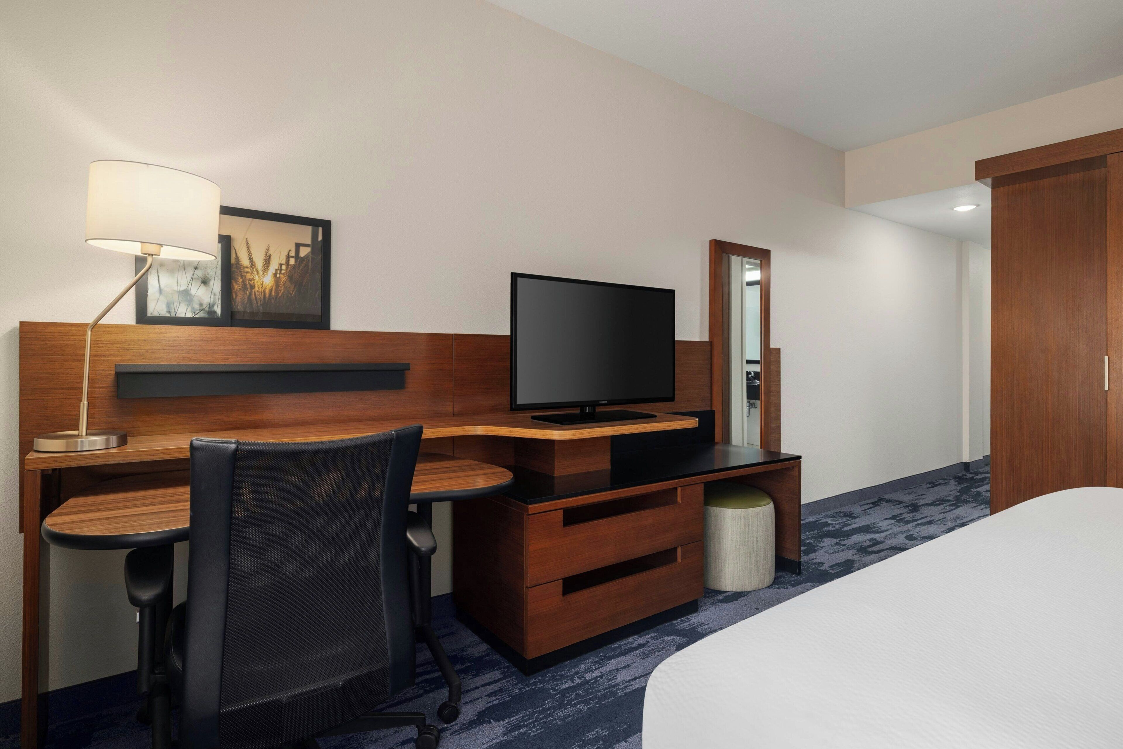 Ein Hotelzimmer mit Holztisch, Fernseher, Stuhl, Bett und Lampe.