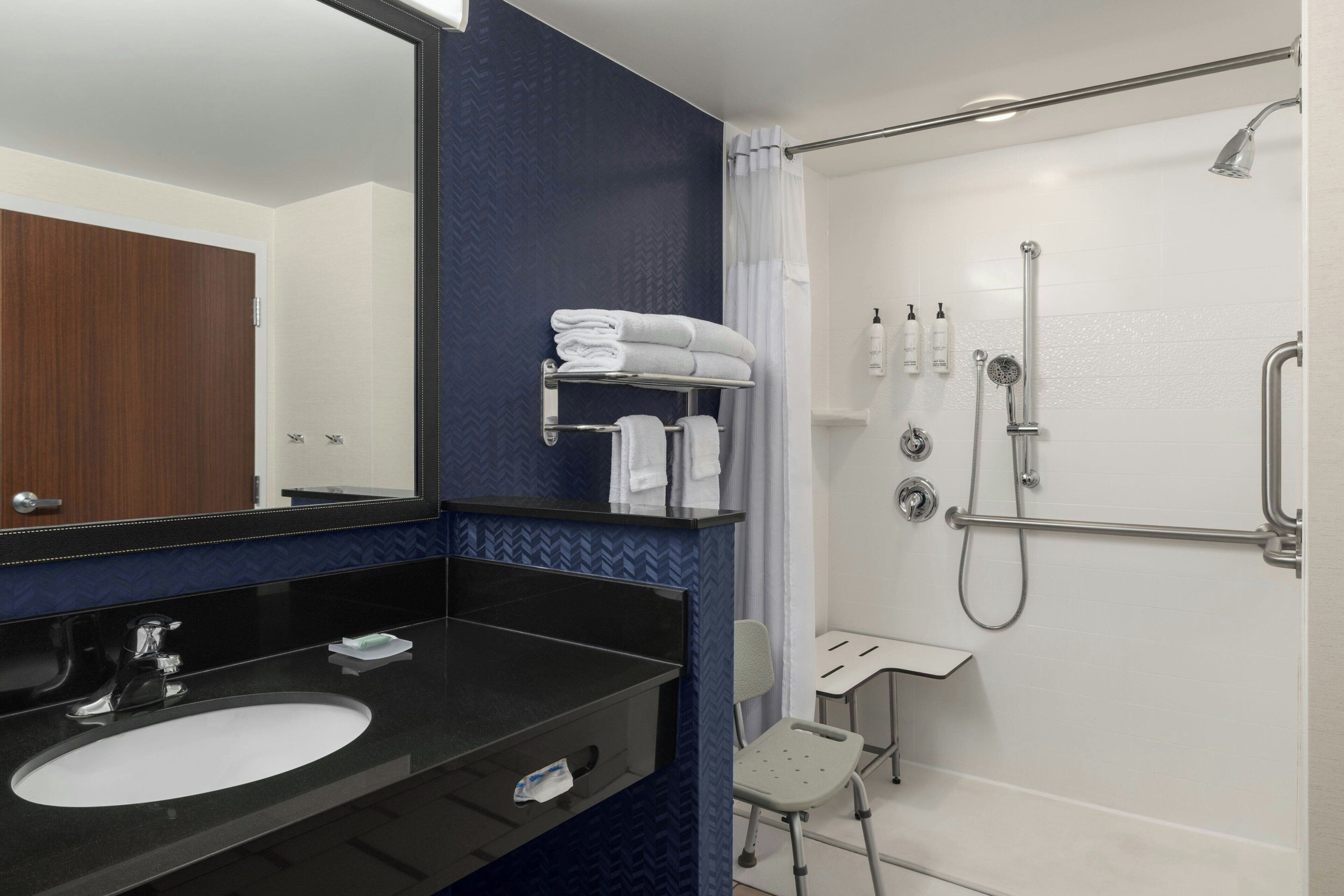 Une salle de bain avec un lavabo noir, un miroir, une douche avec un pommeau de douche amovible et un porte-serviettes.