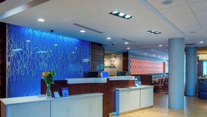 Un espace d’accueil moderne avec un mur illuminé de lumière bleue, un comptoir d’accueil et un coin salon offrant une vue sur le paysage urbain.