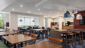 Un comedor de hotel con varias mesas y sillas, una zona de bar e iluminación colgante.