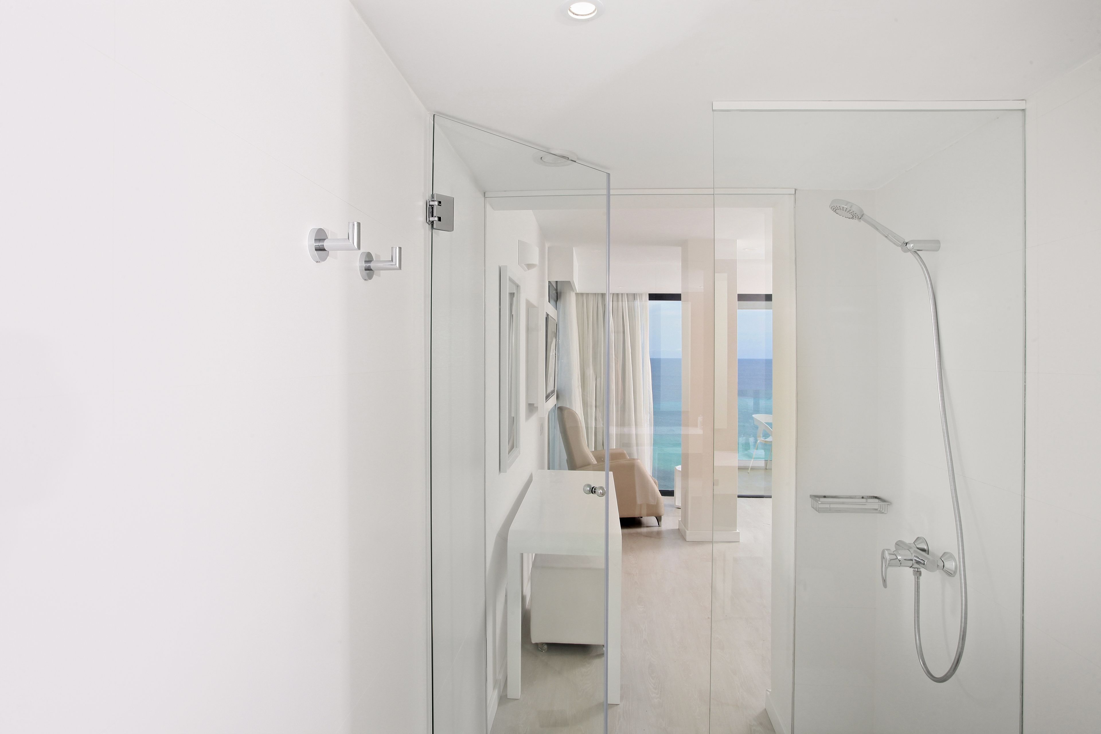 A modern bathroom with a glass shower enclosure, a white vanity, and a view of the sea through the window.