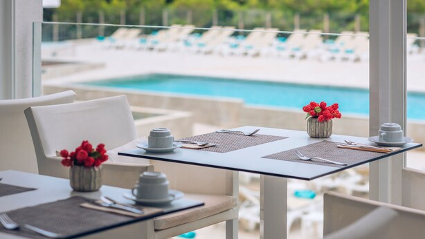A dining table with a view of a pool and lounge chairs.