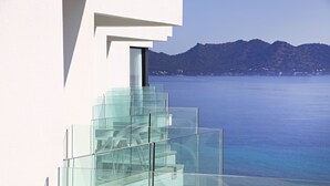 A modern building with a glass staircase leading to a balcony overlooking a body of water and a mountainous landscape.