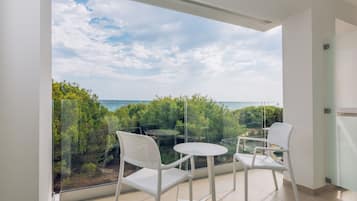 A balcony with two white chairs and a small table, overlooking a coastal landscape with trees and the sea.