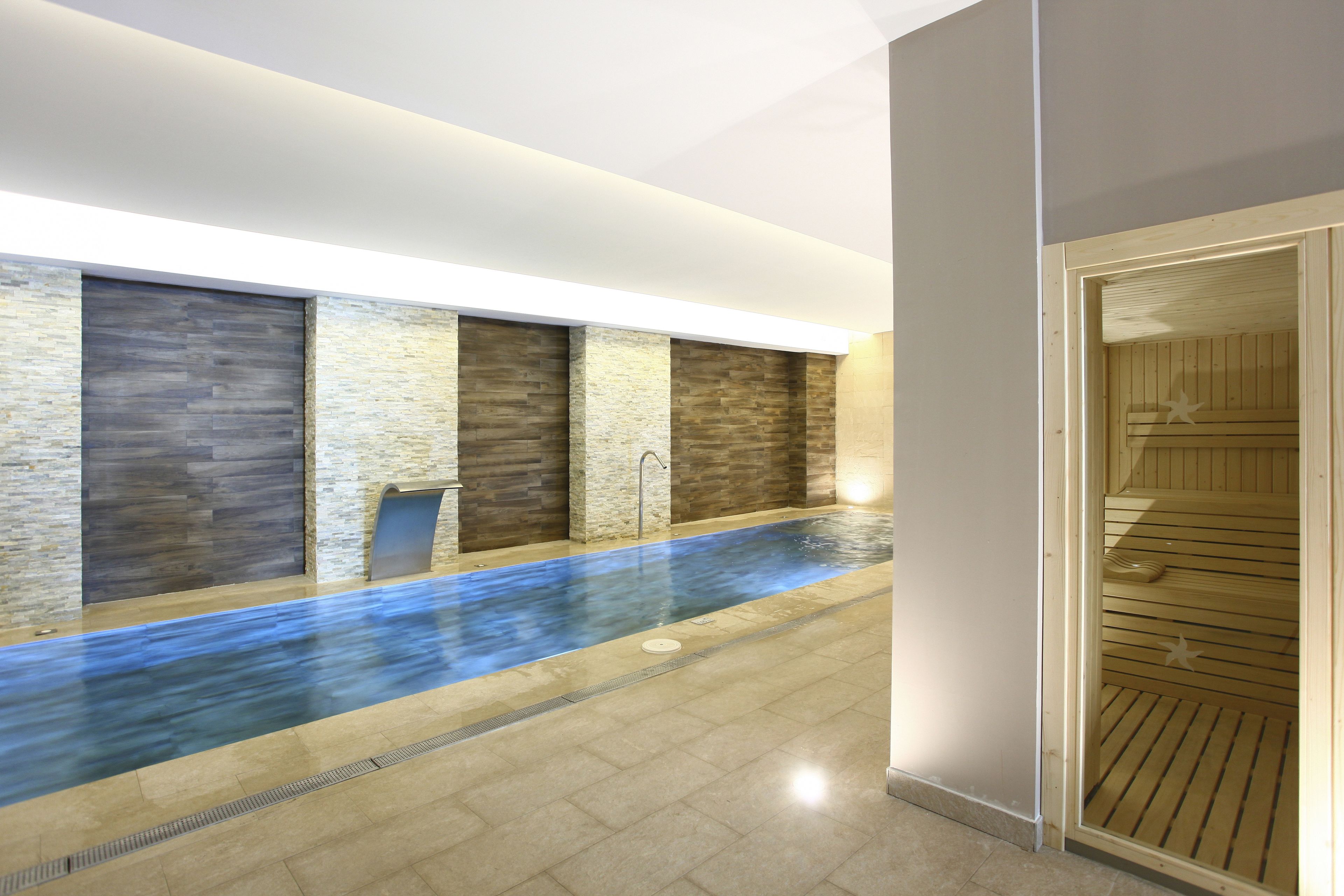 A modern indoor pool with stone walls and a wooden sauna area.